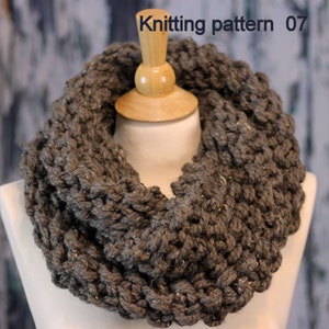 May include: A gray knitted infinity scarf with a chunky knit texture. The scarf is displayed on a mannequin.