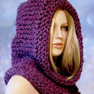 May include: A purple knitted cowl with a hood. The cowl is made of a soft, chunky yarn and has a loose, drapey fit.