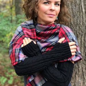 May include: A woman wearing black fingerless gloves with a red, black, and blue plaid scarf. The scarf is tied around her neck and draped over her shoulders.