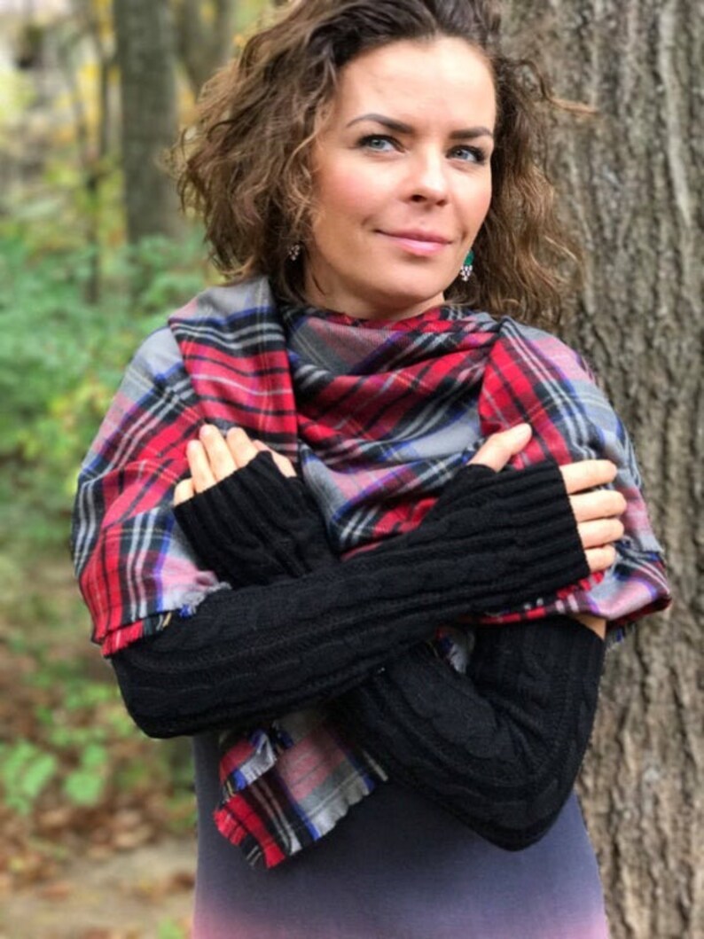 May include: A woman wearing black fingerless gloves with a red, black, and blue plaid scarf. The scarf is tied around her neck and draped over her shoulders.