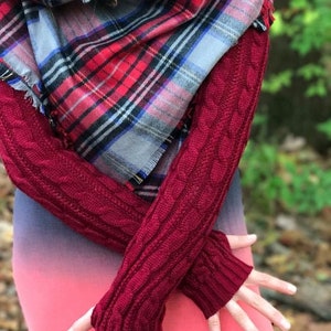 May include: Red and blue plaid scarf with frayed edges and a pair of burgundy knitted arm warmers with a cable knit pattern.
