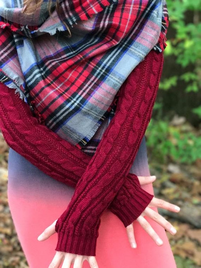 May include: Red and blue plaid scarf with frayed edges and a pair of burgundy knitted arm warmers with a cable knit pattern.
