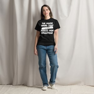 May include: Black t-shirt with the text "THE MAGIC WAND THAT MAKES MEN DISAPPEAR" and a graphic of a pregnancy test. The person is wearing blue jeans and white sneakers.