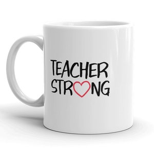 May include: White ceramic mug with the words "TEACHER STRONG" in black lettering and a red heart symbol. The mug has a curved handle and is designed for hot beverages. A perfect gift for teachers.