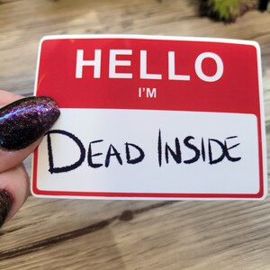 May include: A red and white name tag with the text "HELLO I'M DEAD INSIDE" written in black marker.