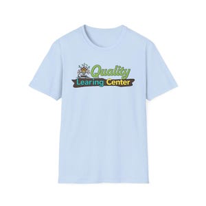Könnte beinhalten: Hellblaues T-Shirt mit Rundhalsausschnitt. Das Shirt zeigt eine farbenfrohe Grafik mit der Aufschrift "Quality Learing Center". Die Grafik enthält ein Haus, Blätter und Text in Grün und Gelb.