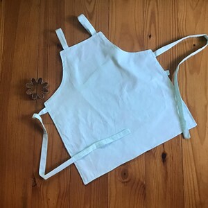 May include: A light blue apron with adjustable straps. The apron is made of a soft, lightweight fabric.