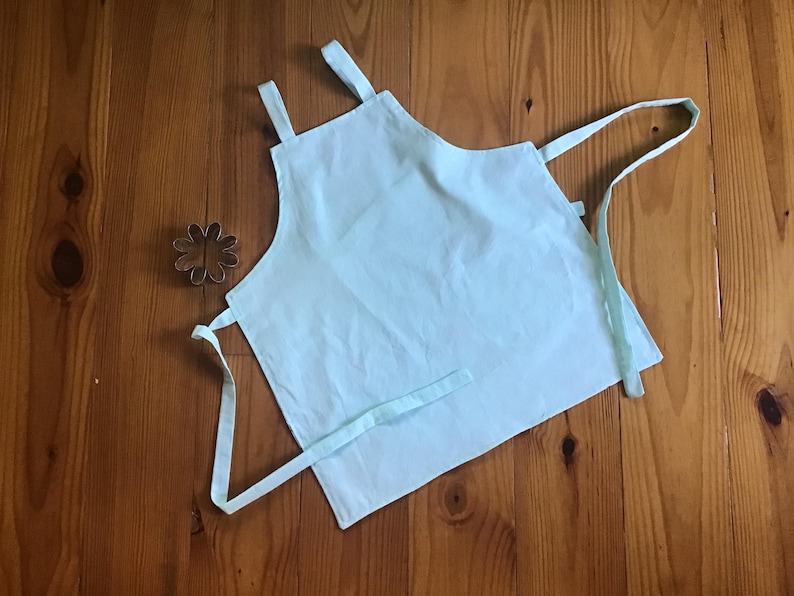 May include: A light blue apron with adjustable straps. The apron is made of a soft, lightweight fabric.