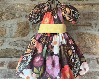 May include: A floral print dress with a yellow belt. The dress features a dark brown background with large flowers in shades of pink, orange, and white. The dress has short, puffed sleeves.