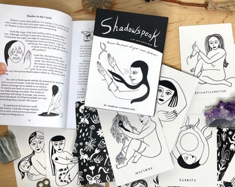 Può includere: Un mazzo di carte oracle in bianco e nero chiamato "Shadowspeak: Access the power of your inner darkness" con carte che presentano illustrazioni di figure in varie pose. Le carte sono disposte su una superficie di legno con un libro e altri oggetti.