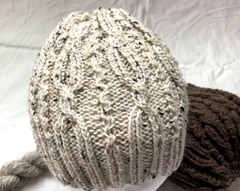 May include: A white knitted hat with a cable knit pattern. The hat is on a white mannequin head.