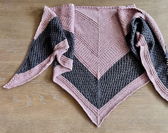 May include: A knitted shawl in a triangular shape, featuring a color-blocked design. The shawl has a dark gray section and a mauve section, with a mauve border. The texture of the knit is visible, and the shawl is displayed on a wooden surface.