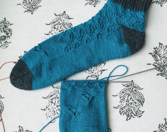 May include: A pair of teal blue knitted socks with a black heel and toe. One sock is fully knitted and the other is partially knitted.