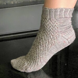 May include: A pair of grey ankle socks with a lacy pattern. The socks are knitted and have a subtle sheen.