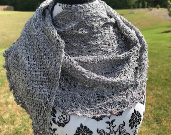 May include: A gray and silver knitted shawl with a delicate lace border and small pink beads. The shawl is draped over a black mannequin.