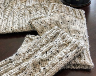 May include: A set of knitted beige and white mittens and a matching beanie with a cable knit pattern. The beanie has a slouchy fit. The mittens and beanie are made with a speckled yarn.