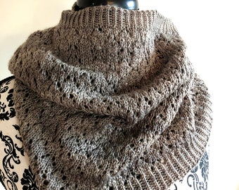 May include: A gray knitted cowl scarf with a textured, openwork design. The scarf is displayed on a black and white patterned mannequin head. The cowl is made of a soft, warm material, perfect for cold weather.