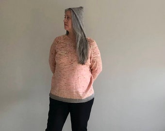 May include: A woman wearing a pink speckled sweater with a gray knit hat. The sweater has a gray trim around the bottom.