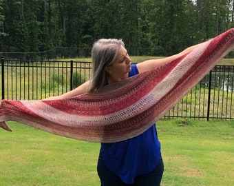 May include: A woman wearing a blue shirt and jeans is holding a red, white, and brown striped knitted shawl. The shawl is draped over her shoulders and arms, and she is holding it out in front of her.