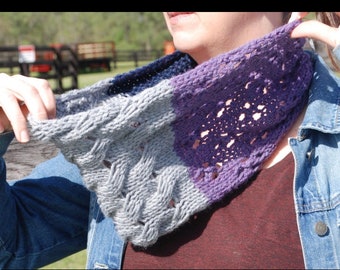 May include: A knitted cowl with a gray, blue, and purple color pattern. The cowl is made with a cable stitch and a lacy stitch.