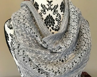 May include: A gray and white knitted infinity scarf with a delicate lace pattern. The scarf is draped over a black and white patterned mannequin.