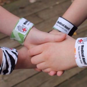 May include: Medical alert wristbands in various patterns and colors. One band features a green and white design, another a black and white zebra print, and two others are white with the words "Medical Alert!" and a red cross symbol. The text "See reverse side" is also printed on the white bands.