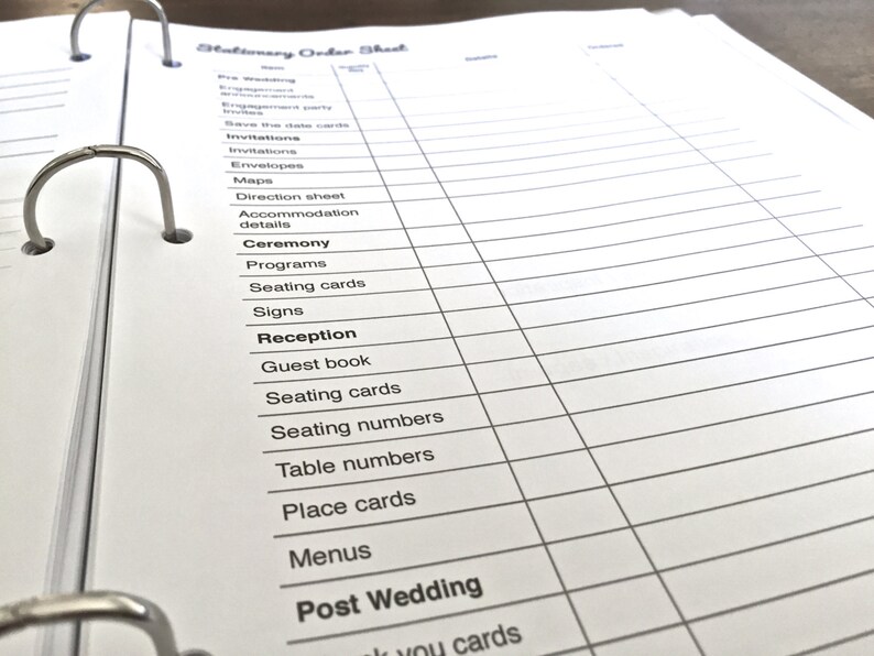 Op de afbeelding: Een wit bestelformulier voor briefpapier met een zwarte ringband. Het formulier bevat een lijst met verschillende artikelen die nodig zijn voor een bruiloft, waaronder uitnodigingen, enveloppen, kaarten, routebeschrijvingen, accommodatiegegevens, ceremonieprogramma's, plaatskaarten, borden, gastenboek voor de receptie, plaatskaarten, tafelnummers, tafelkaarten, menu's en bedankkaartjes na de bruiloft.