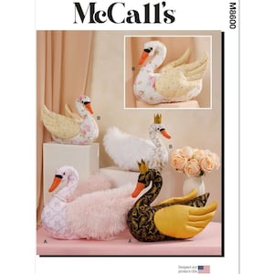 May include: McCall's sewing pattern featuring swan-shaped plushies in various designs. The swans have floral, gold, and black patterns, with orange beaks and some wearing crowns. The image includes the text "Designed and printed in USA."