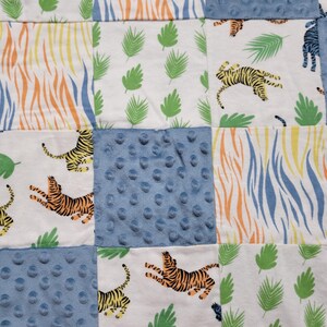 May include: A patchwork quilt with a variety of patterns, including stripes, leaves, and polka dots. The quilt features a blue, white, and orange color scheme with images of tigers throughout.