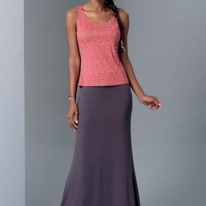 May include: A woman is wearing a sleeveless, coral-colored tank top with a white print and a long, dark purple skirt. The skirt is fitted at the waist and flows out to a wide hem.