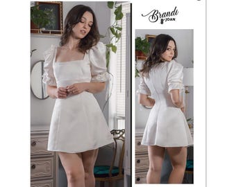 Könnte beinhalten: Ein weißes Kleid mit quadratischem Ausschnitt und Puffärmeln. Das Kleid hat ein tailliertes Oberteil und einen ausgestellten Rock. Das Kleid wird an einem Model in einem Studio gezeigt.
