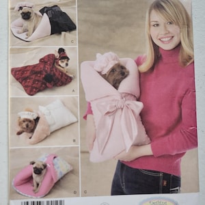 May include: A Simplicity sewing pattern envelope, number 2744, featuring illustrations of small dogs in handmade sleeping bags and hats. The cover displays four variations of pet bedding and accessories, including a pink swaddle with a large bow.