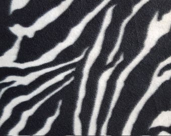 May include: Close-up of a black and white zebra print fabric. The pattern features bold, irregular black stripes against a white background. The fabric has a soft, textured appearance, suggesting a plush material.
