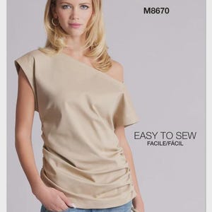 May include: A sewing pattern envelope for McCall's M8670, featuring a beige one-shoulder top with short sleeves and side ruching. The text reads McCall's, M8670, EASY TO SEW, FACILE/FÁCIL, and Designed and printed in USA with a small American flag icon.