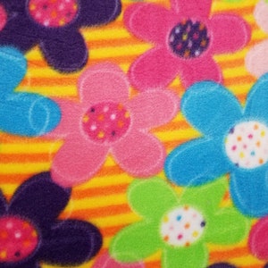 May include: Close-up of a colorful fleece fabric featuring large, stylized flowers in shades of pink, blue, green, and purple. The flowers have white centers with colorful polka dots. The background has orange and yellow stripes.