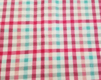 May include: A close-up of a fabric with a checkered pattern. The pattern features a grid of white, red, teal, and gray squares. The fabric appears to be soft and possibly used for clothing or home decor.