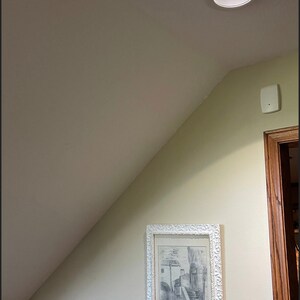 May include: A recessed ceiling light with a bright, focused beam. The light is set in a white circular housing. A framed black and white print of a European street scene hangs on the wall. The wall is painted a light green color.