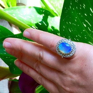 May include: A silver ring with a large oval opal gemstone surrounded by a halo of smaller diamonds.