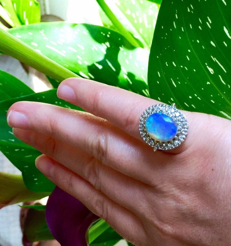 May include: A silver ring with a large oval opal gemstone surrounded by a halo of smaller diamonds.