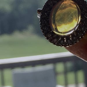 May include: A gold ring with a large, round, yellow gemstone surrounded by a halo of small, black gemstones.