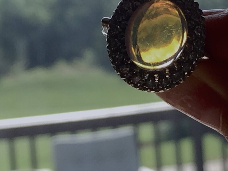 May include: A gold ring with a large, round, yellow gemstone surrounded by a halo of small, black gemstones.