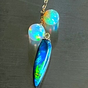 May include: A gold chain necklace with two iridescent opal beads and a long, teardrop-shaped opal pendant with blue, green, and black hues.