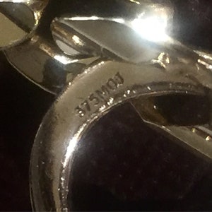 May include: Close-up of a gold-toned metal chain with the inscription "875M01" visible.