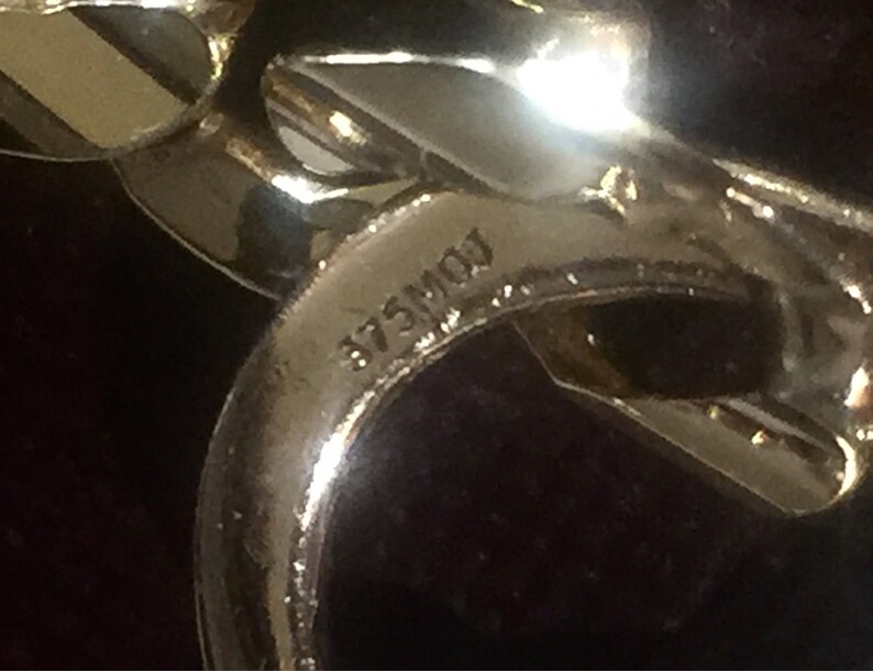 May include: Close-up of a gold-toned metal chain with the inscription "875M01" visible.
