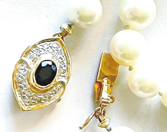 May include: A pearl necklace with a gold clasp and a decorative pendant. The pendant has a gold frame with clear stones and a black oval stone in the center. The pearls are large and round.