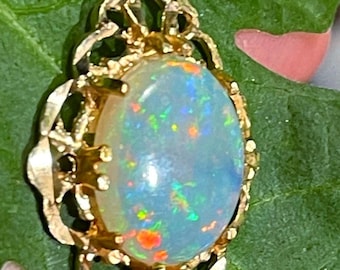 May include: A gold pendant featuring a white opal with iridescent rainbow flashes set in a delicate filigree design.