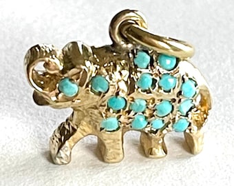 Könnte beinhalten: Ein goldener Elefanten-Anhänger mit türkisfarbenen Steinen, die in die Oberfläche eingefasst sind. Der Anhänger hat oben eine Schlaufe zum Anbringen an einer Halskette oder einem Armband.