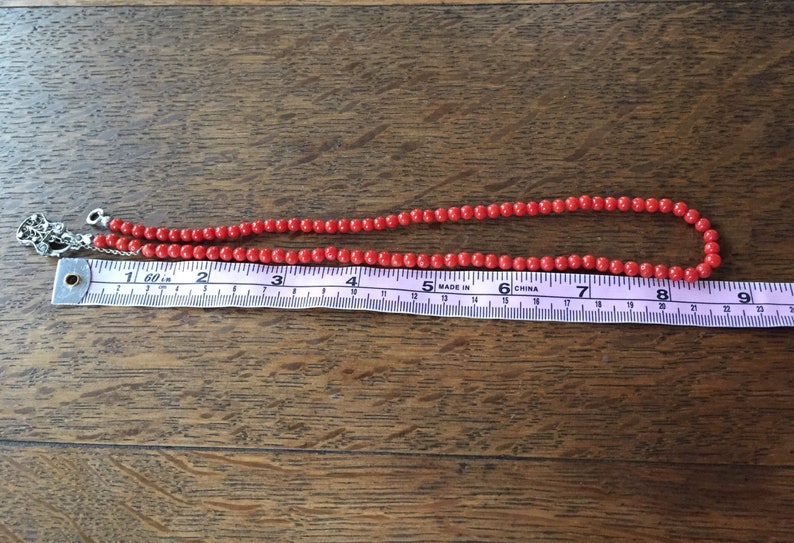 Puede incluir: Un collar de cuentas de coral rojo con un cierre de plata, que mide 20 cm de largo.