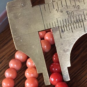 Puede incluir: Primer plano de un collar de cuentas de coral que se mide con una pinza de calibre de lat&oacute;n. La pinza muestra medidas en pulgadas, con la cuenta midiendo aproximadamente 1/4 de pulgada de di&aacute;metro.