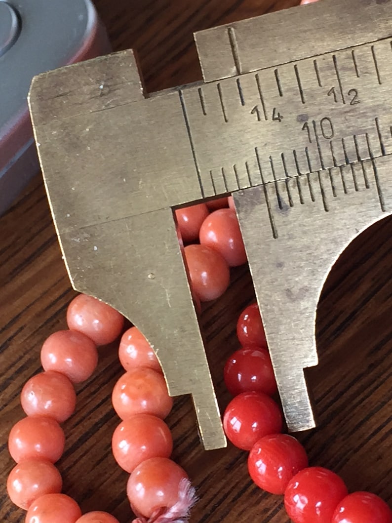 Puede incluir: Primer plano de un collar de cuentas de coral que se mide con una pinza de calibre de lat&oacute;n. La pinza muestra medidas en pulgadas, con la cuenta midiendo aproximadamente 1/4 de pulgada de di&aacute;metro.